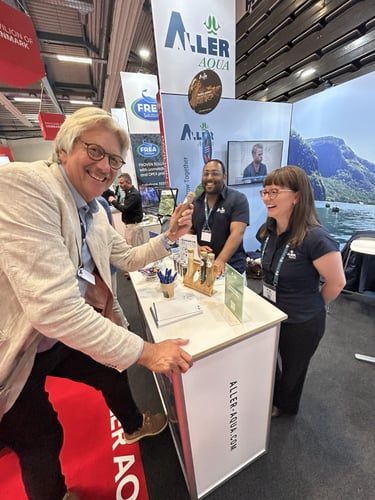 to menn og en kvinne som står på en stand på en AquaNor-messe, mannen viser tommel opp