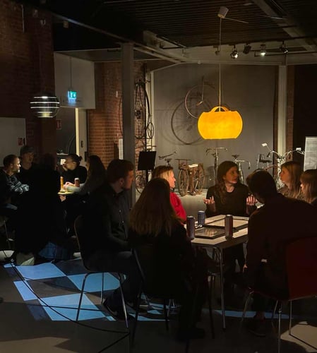 mennesker som sitter rundt et bord og diskuterer inne på teknisk museum i oslo, det er ganske mørkt i lokalet