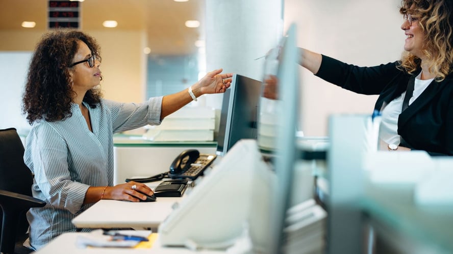 En kvinne rekker noe til en annen kvinne over en skillevegg på et kontor