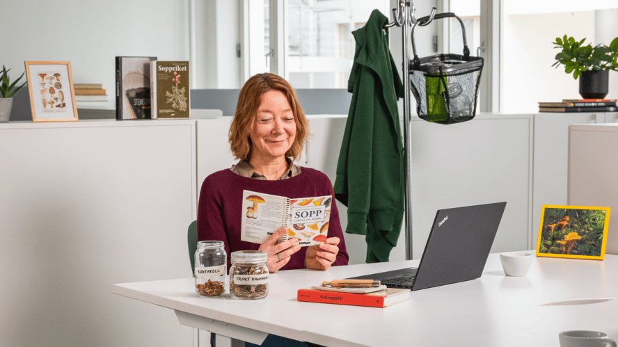 En dame sitter foran en kontorpult og leser en bok om sopp